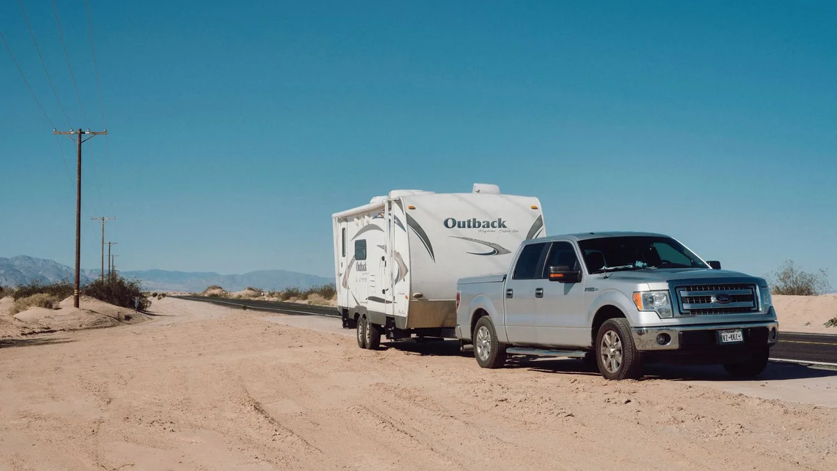 Truck towing a trailer loaded with gear on an open road, representing motorcycle touring with trailer support