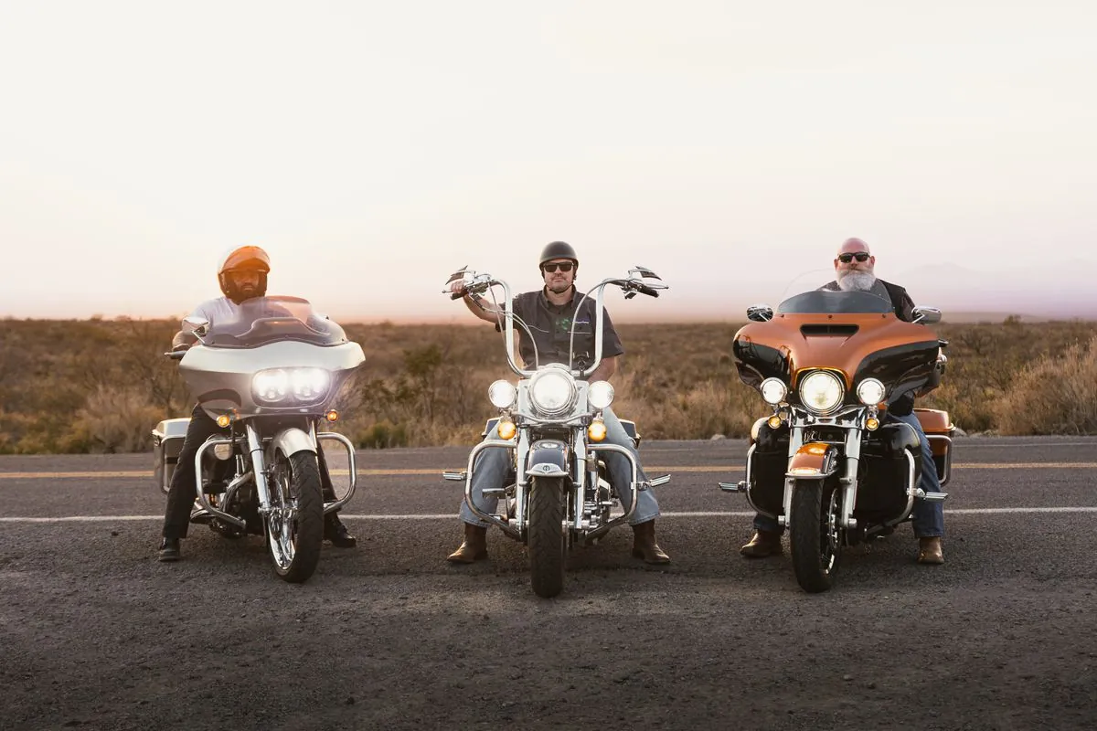 Three motorcycle riders on a scenic road at sunset