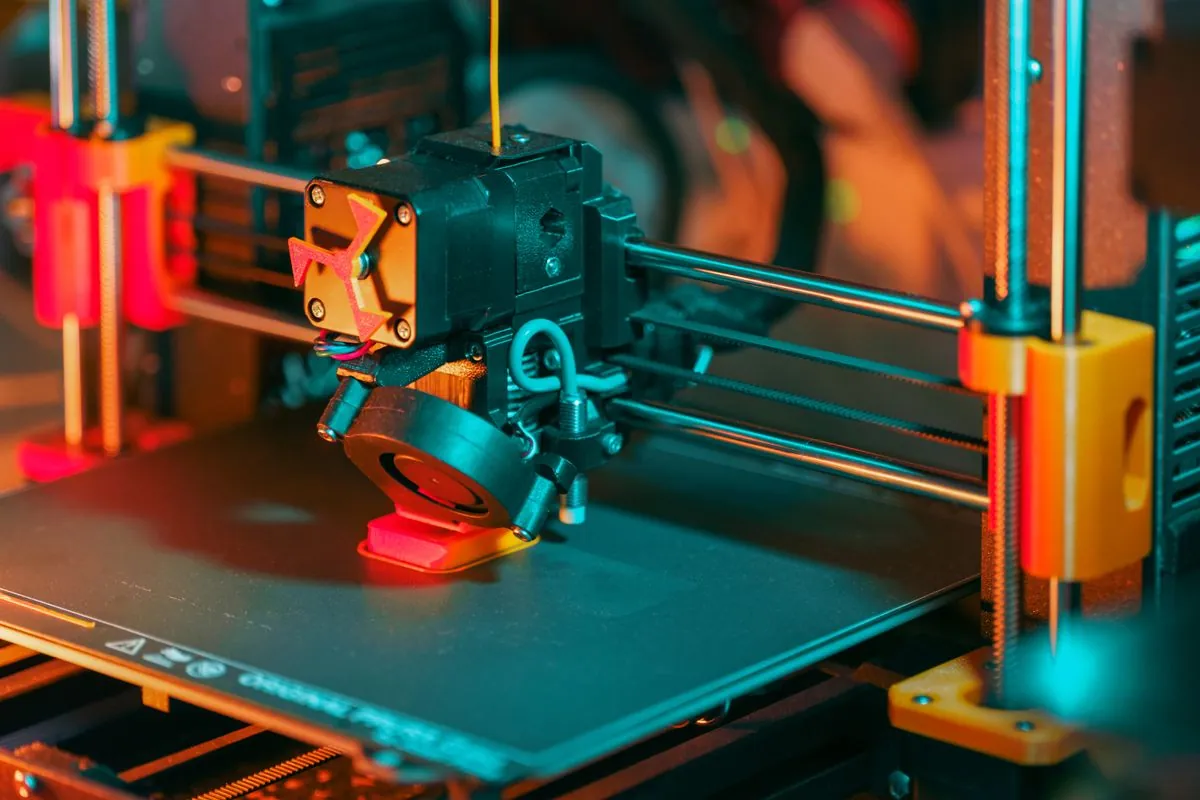 Budget 3D printer on a workbench printing a small object with filament spool visible