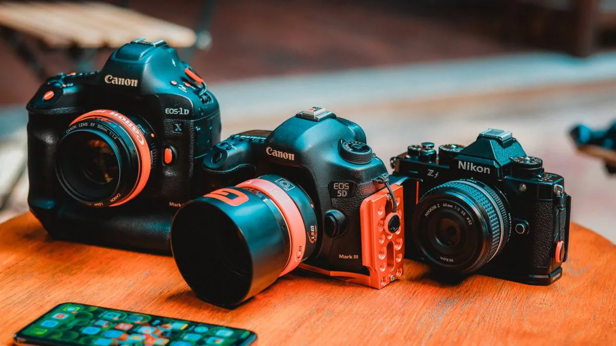 Professional mirrorless cameras arranged on a wooden table for comparison, representing the Canon R1, Sony A1 II, and Nikon Z6 III